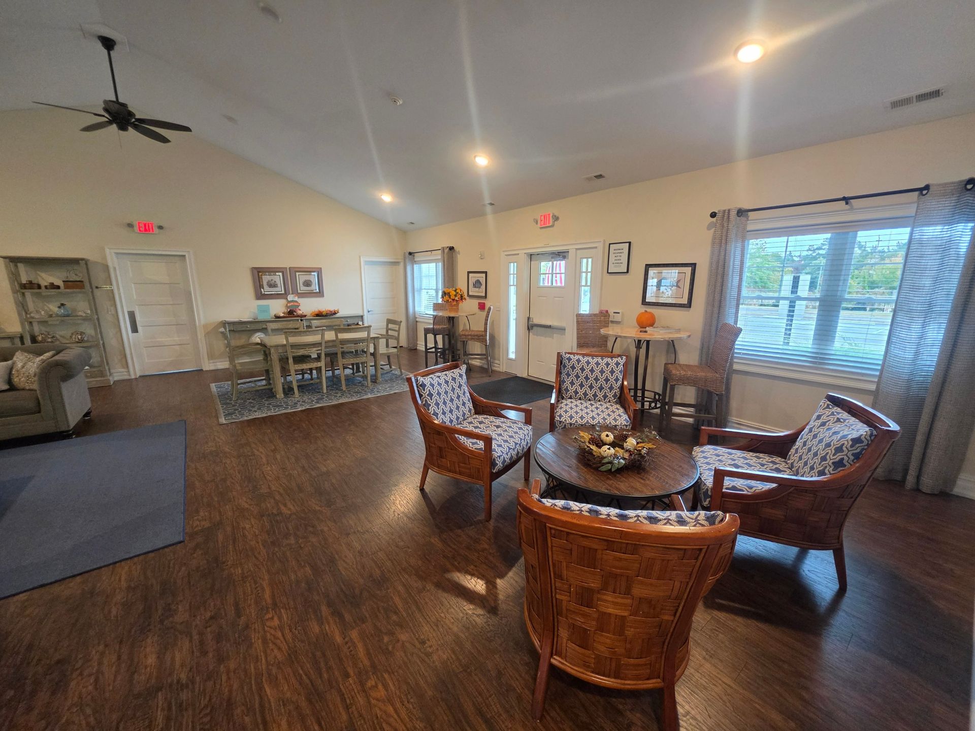 Woven armchairs around a round table near the clubhouse entrance, with a dining table beyond