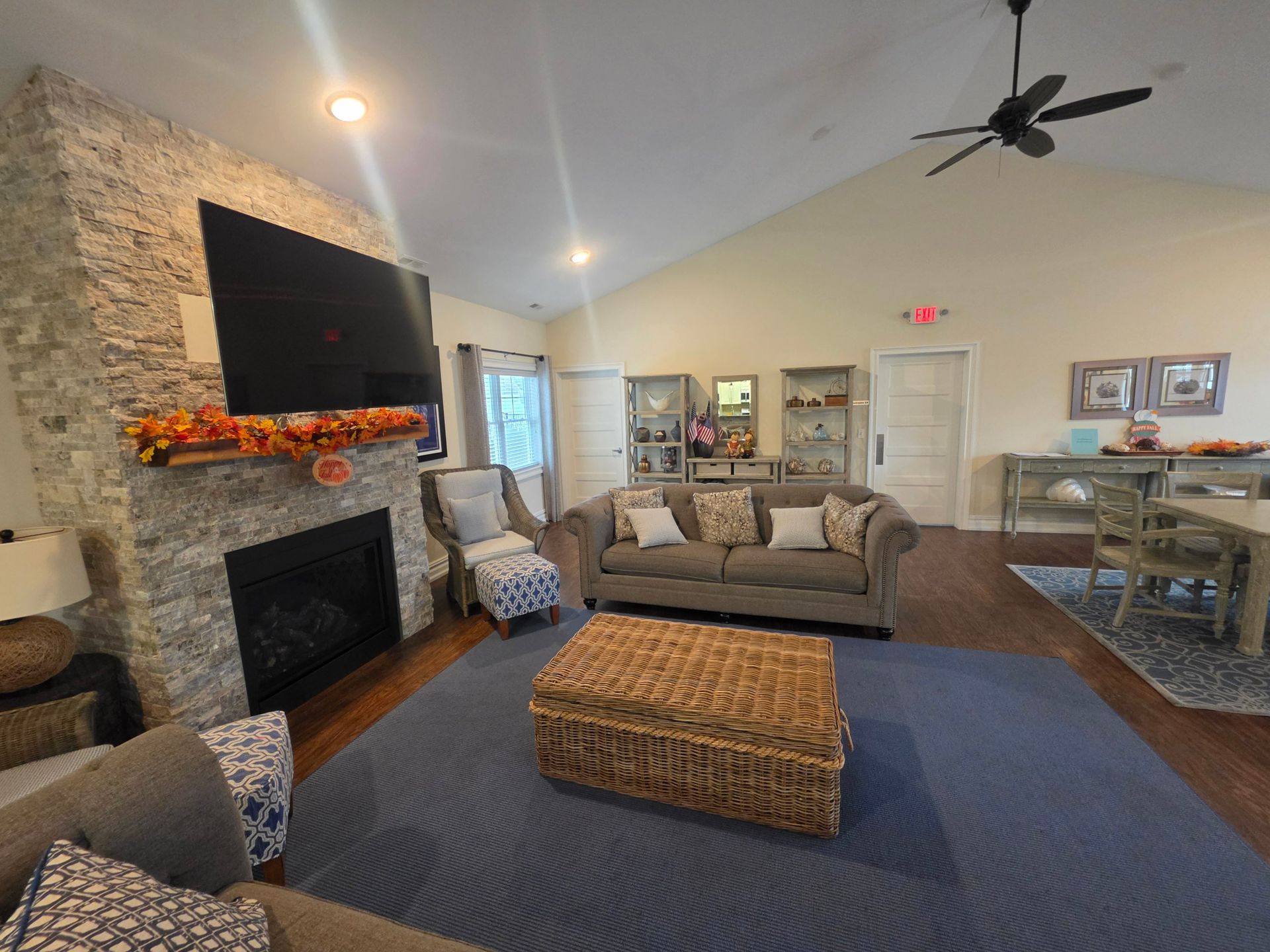 Stone fireplace with a mounted TV, sofa, wicker chest and blue area rug in the clubhouse