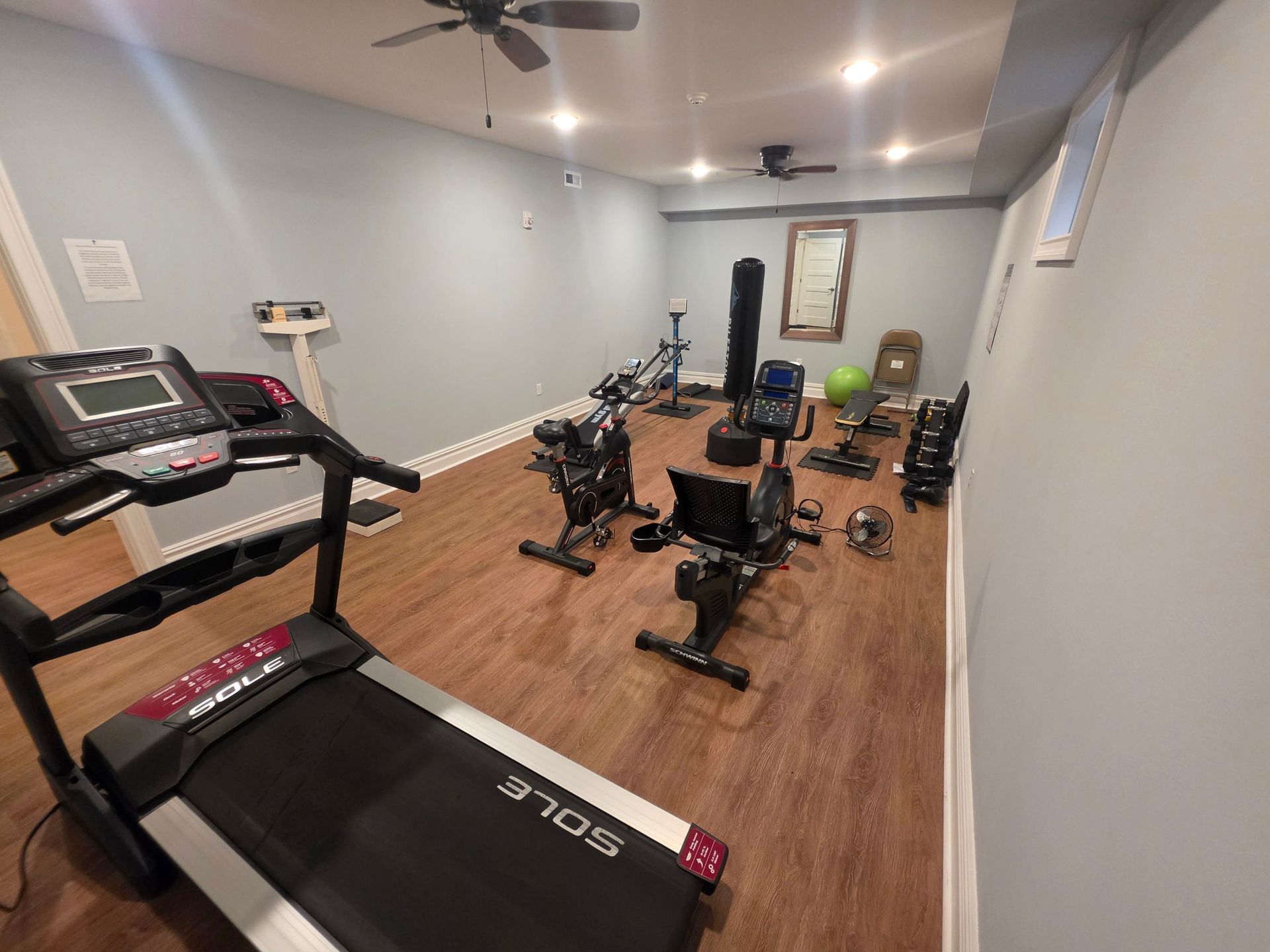 Fitness room with a treadmill, recliner bike, spin bike, weight bench and dumbbells