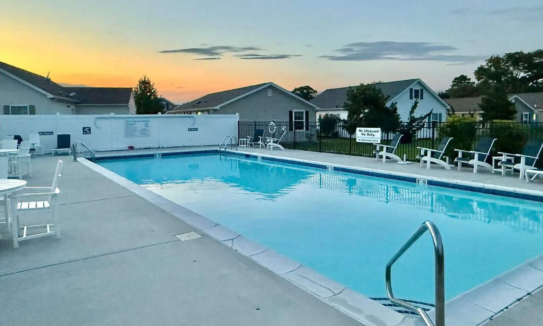 The community pool with white patio tables and an umbrella